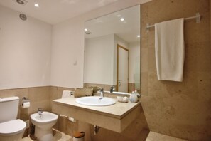 A bathroom with a toilet, bidet, sink, and a large mirror.