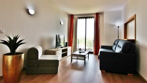 A living room with a sofa, a coffee table, a TV, and a potted plant. - Residences Golf Club - Pool and Tenis Court (Vilamoura)