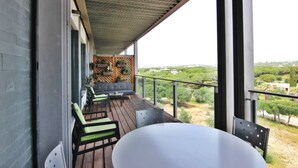 A balcony with a wooden floor, a white table, and two green and black chairs. - Residences Golf Club - Pool and Tenis Court (Vilamoura)