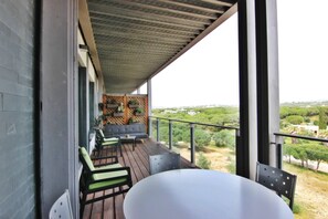 A balcony with a wooden floor, a white table, and two green and black chairs.