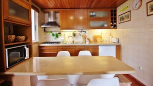 A kitchen with wooden cabinets, a microwave, a sink, and a dining table with chairs. - Solar do Golfe - Pools & Old Village (Vilamoura)
