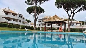 A swimming pool with a gazebo, trees, and modern buildings in the background. - Solar do Golfe - Pools & Old Village (Vilamoura)