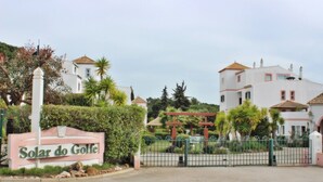 A sign reading "Solar do Golfe" with a gated entrance, surrounded by lush greenery and buildings with tiled roofs. - Solar do Golfe - Pools & Old Village (Vilamoura)