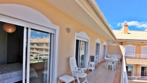 Un balcon avec des chaises blanches et une petite table, une porte-fenêtre coulissante et un sol carrelé.