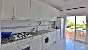 Une cuisine moderne avec des meubles blancs, une cuisinière à gaz, un lave-linge et un balcon doté d’un espace salon extérieur.