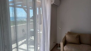 A room with a beige sofa, a white curtain, and an air conditioning unit mounted on the wall. - Bleu Horizon en Tout Compris (Linguizzetta)