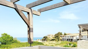 A patio with a table and chairs, overlooking a beach and a building. - Bleu Horizon en Tout Compris (Linguizzetta)