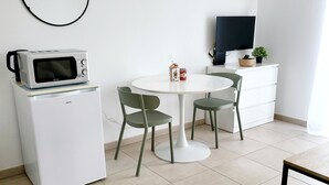 A compact living space with a white refrigerator, a microwave, a small dining table with two chairs, a television on a stand, and a potted plant. - Bleu Horizon en Tout Compris (Linguizzetta)