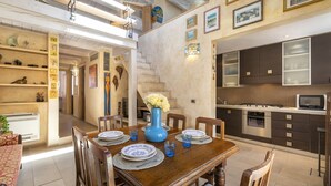 Un comedor con una mesa de madera dispuesta para cuatro personas, rodeada de sillas. En la mesa, un jarrón azul con flores.