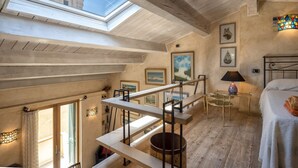 Una habitación con techos altos, tragaluces, una cama, una mesita y obras de arte en las paredes.