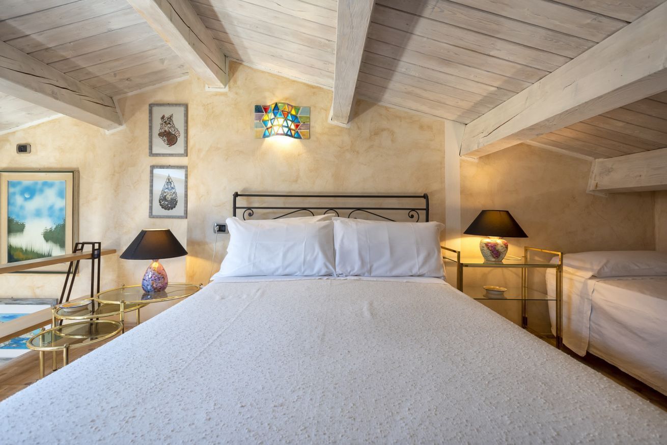 Een slaapkamer met een groot bed, twee nachtkastjes met lampen, een schilderij aan de muur en een plafond met zichtbare balken.