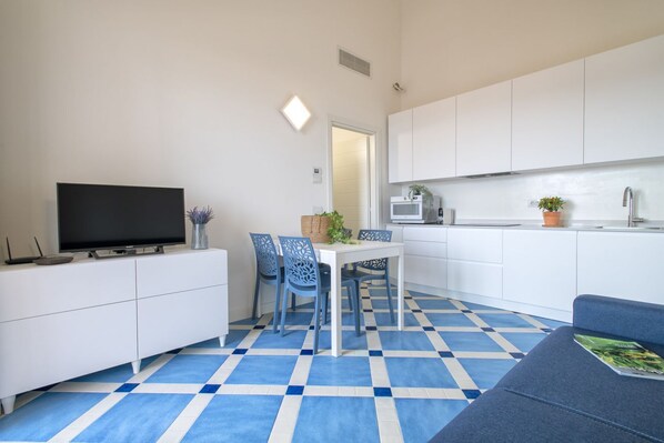 A compact living space with a TV, dining table, chairs, and a kitchenette.
