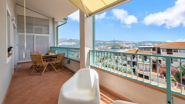 Un balcón con mesa y sillas, una bañera blanca y vistas a un puerto deportivo con barcos.