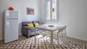 A small, modern kitchen with a white refrigerator, a gray sofa with yellow cushions, a white dining table with chairs, and a patterned floor. - Casa Libeccio. Apartment in the center with A/C and free wi-fi. (Alghero)