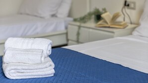 A neatly made bed with a blue quilt, a stack of white towels, and a bedside table with an open book and a lamp. - Casa Libeccio. Apartment in the center with A/C and free wi-fi. (Alghero)