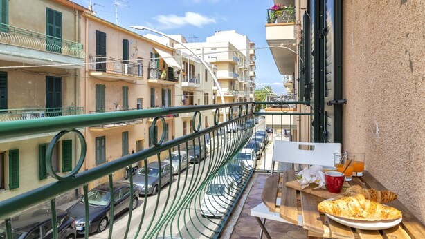A balcony with a table set for breakfast, overlooking a street with parked cars and buildings. - Casa Libeccio. Apartment in the center with A/C and free wi-fi. (Alghero)