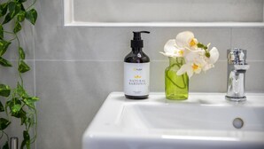 Ein Waschtisch mit einer Flasche natürlicher Sardinien-Seife und einer Vase mit weißen Blumen.