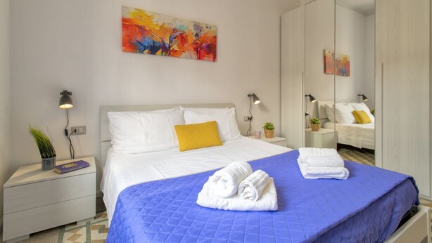 Ein Hotelzimmer mit einem großen Bett, einem Spiegel, einem Nachttisch mit Lampe und einem Gemälde an der Wand.