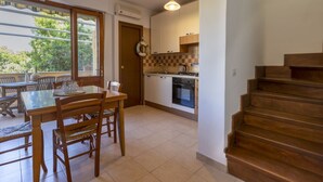 A compact kitchen with a dining area, a wooden staircase, and a view of the outdoors. - Dea Fertilia. Terraced house few steps from the sea. (Fertilia)