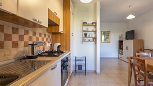 A modern kitchen with a gas stove, oven, and a coffee machine. There is a dining area with a table and chairs. - Dea Fertilia. Terraced house few steps from the sea. (Fertilia)