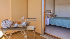 A room with a bed, a dining table with breakfast items, and a view through a glass door. - Dea Fertilia. Terraced house few steps from the sea. (Fertilia)
