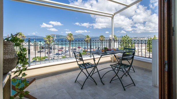 Een balkon met een tafel en stoelen, met uitzicht op een strand en stadsgezicht.