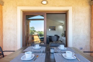 A dining area with a table set for four, a view of the outdoor seating area, and a door leading to another room.
