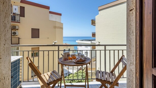 Un balcon avec des chaises en bois et une petite table ronde, offrant une vue sur la côte.