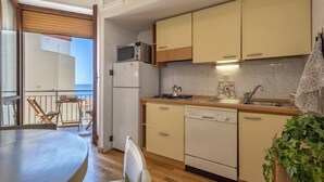 Une cuisine compacte équipée d’un réfrigérateur, d’un four à micro-ondes, d’une cuisinière et d’un lave-vaisselle. Elle comprend un coin repas avec une table et des chaises, ainsi qu’un balcon avec vue.