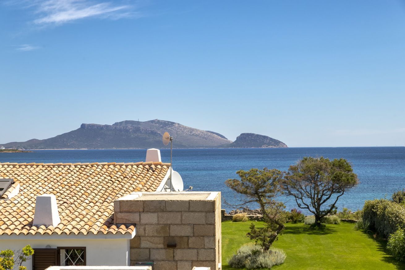 A coastal property with a tiled roof, a satellite dish, and a view of the sea and distant mountains.