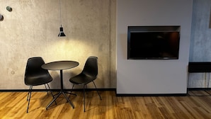 A conference room with a round table, two chairs, a hanging light, and a mounted TV. - ipartment Leverkusen @HOME by Best Western (Leverkusen)
