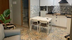 A compact kitchen with white cabinets, a black range hood, and a patterned backsplash. A dining table with chairs is positioned in the center. - Home SEA&DREAMS Beach (Calp)