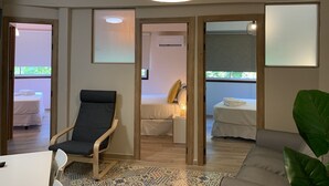 A hotel room with a bed, a chair, a table, and a large plant. There is a window with a view of greenery outside. - Home SEA&DREAMS Beach (Calp)