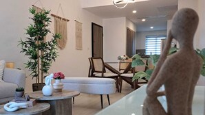 A modern living room with a glass coffee table, a sofa, and a dining area with chairs. - Coral Bay by DR Collection (Punta Cana)