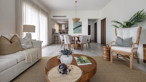 A modern living room with a sofa, coffee table, and a dining area with chairs and a table. - Coral Bay by DR Collection (Punta Cana)