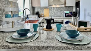 A modern kitchen with granite countertops, a three-tiered glass holder, a coffee maker, and a microwave. - Coral Bay by DR Collection (Punta Cana)