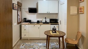 A compact kitchen with white cabinets, a microwave, a coffee maker, and a small dining table with a chair. - Home SEA&DREAMS OldTown IV (Calp)