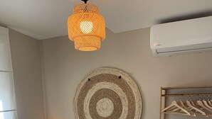 Una cama bien tendida con sábanas blancas y una toalla doblada, un tapiz de pared tejido, un perchero de madera y dos lámparas de noche.