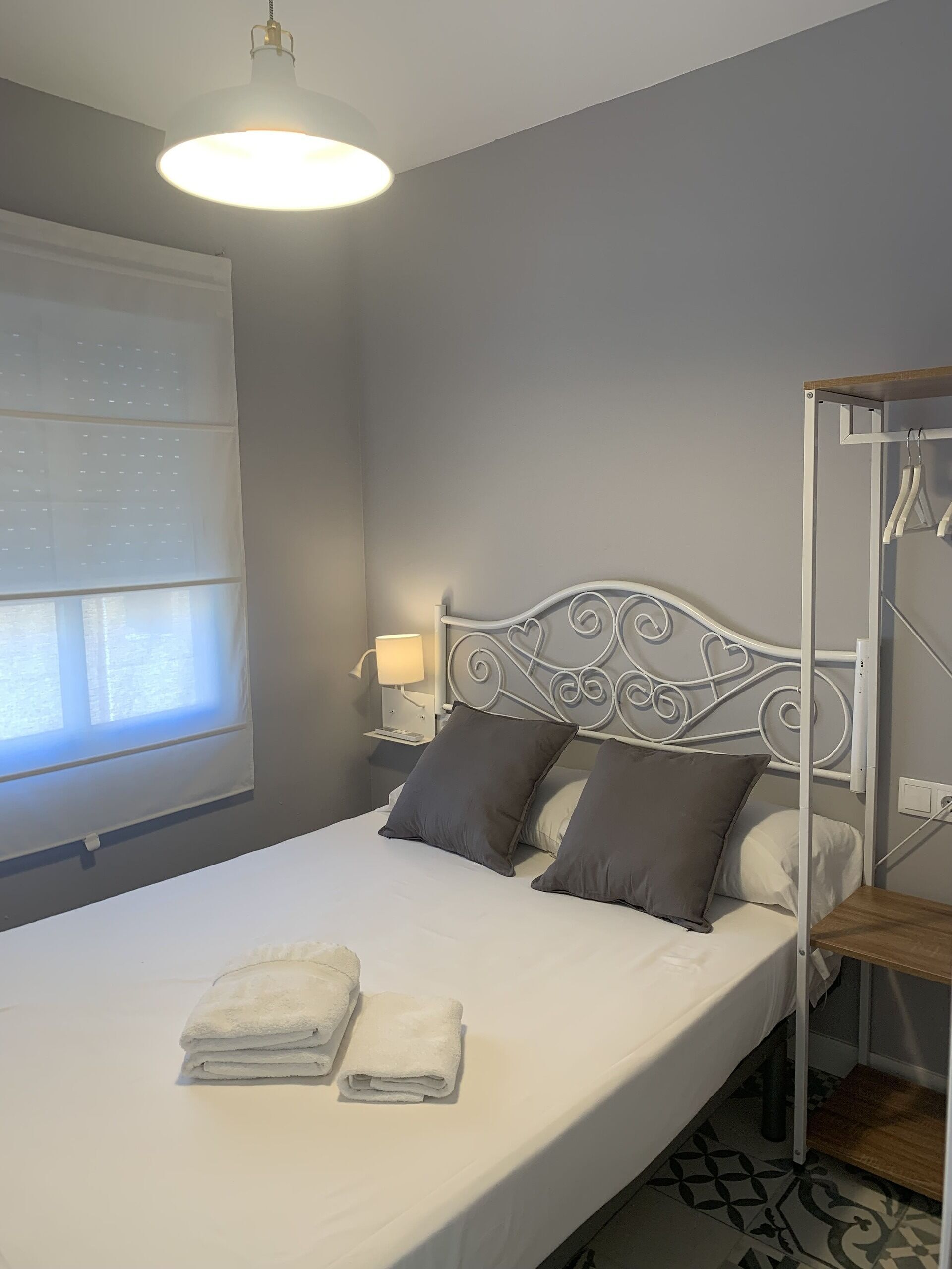 A neatly made bed with two pillows, a bedside lamp, and a window with blinds.