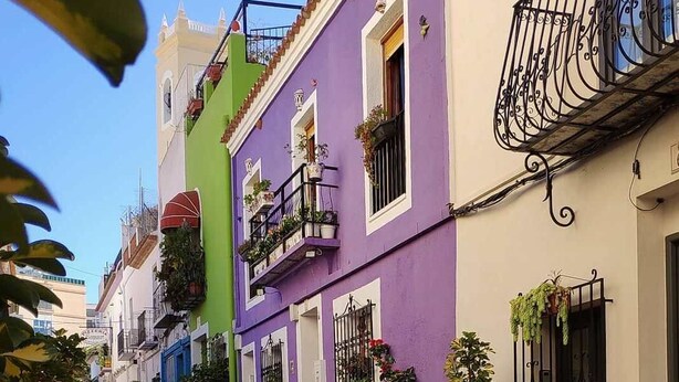 Una calle estrecha bordeada de edificios coloridos, cada uno con balcones y macetas.