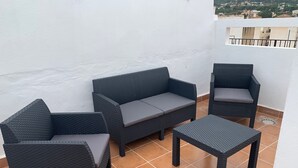 Un balcón con un sofá de mimbre, dos sillones y una mesita, todo con cojines grises.