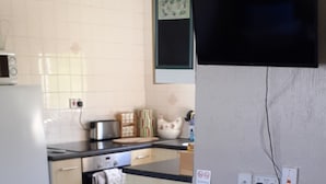 Una cocina con refrigerador, estufa y microondas. Hay un basurero y una alfombra con diseño de hojas.