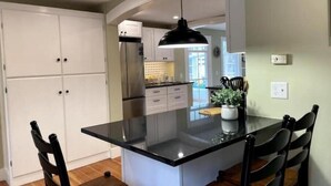 A kitchen with white cabinets, a black countertop, and a hanging light fixture. - Charming Cottage in Jamestown (Jamestown)