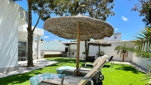 Un espace patio aménagé avec un fauteuil de jardin en osier, une petite table et un parasol en chaume.