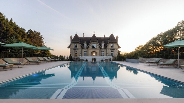 A large rectangular swimming pool with a reflection of a grand building in the background. - Maison Douce Epoque - Deauville (Benerville-sur-Mer)