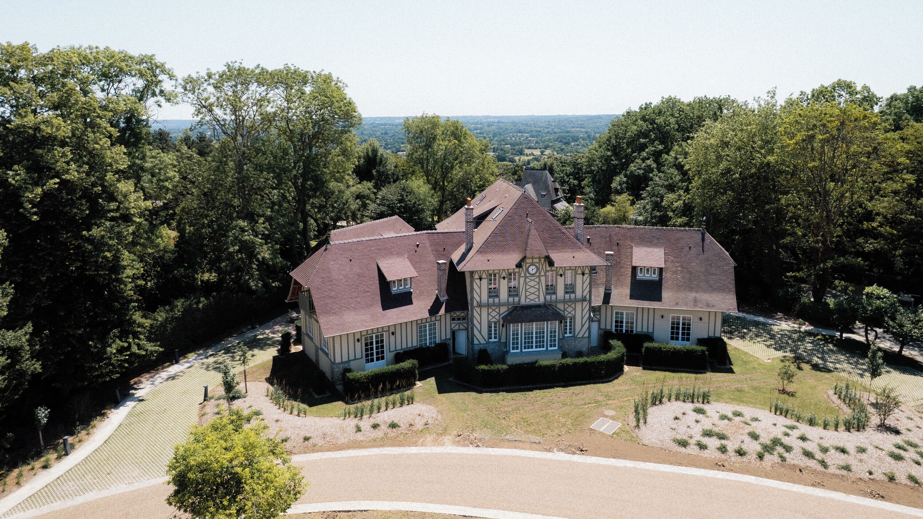 Une grande maison à deux étages, dotée d’une façade symétrique, de nombreuses cheminées et d’une pelouse bien entretenue.