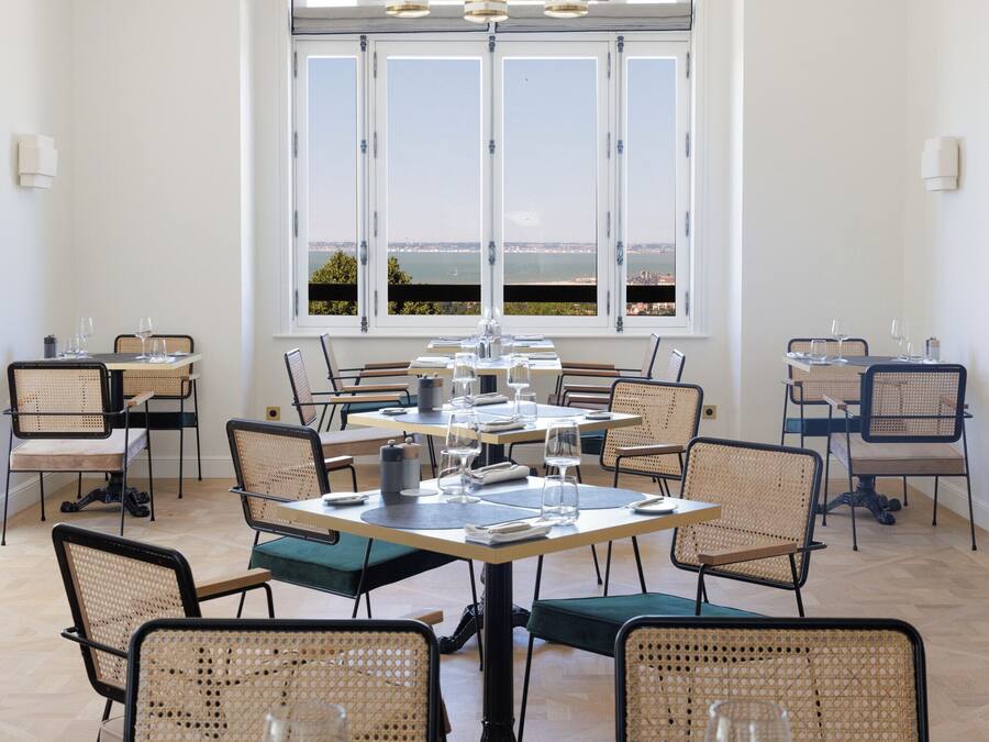 A dining area with multiple tables, chairs, and a large window offering a view of the sea.