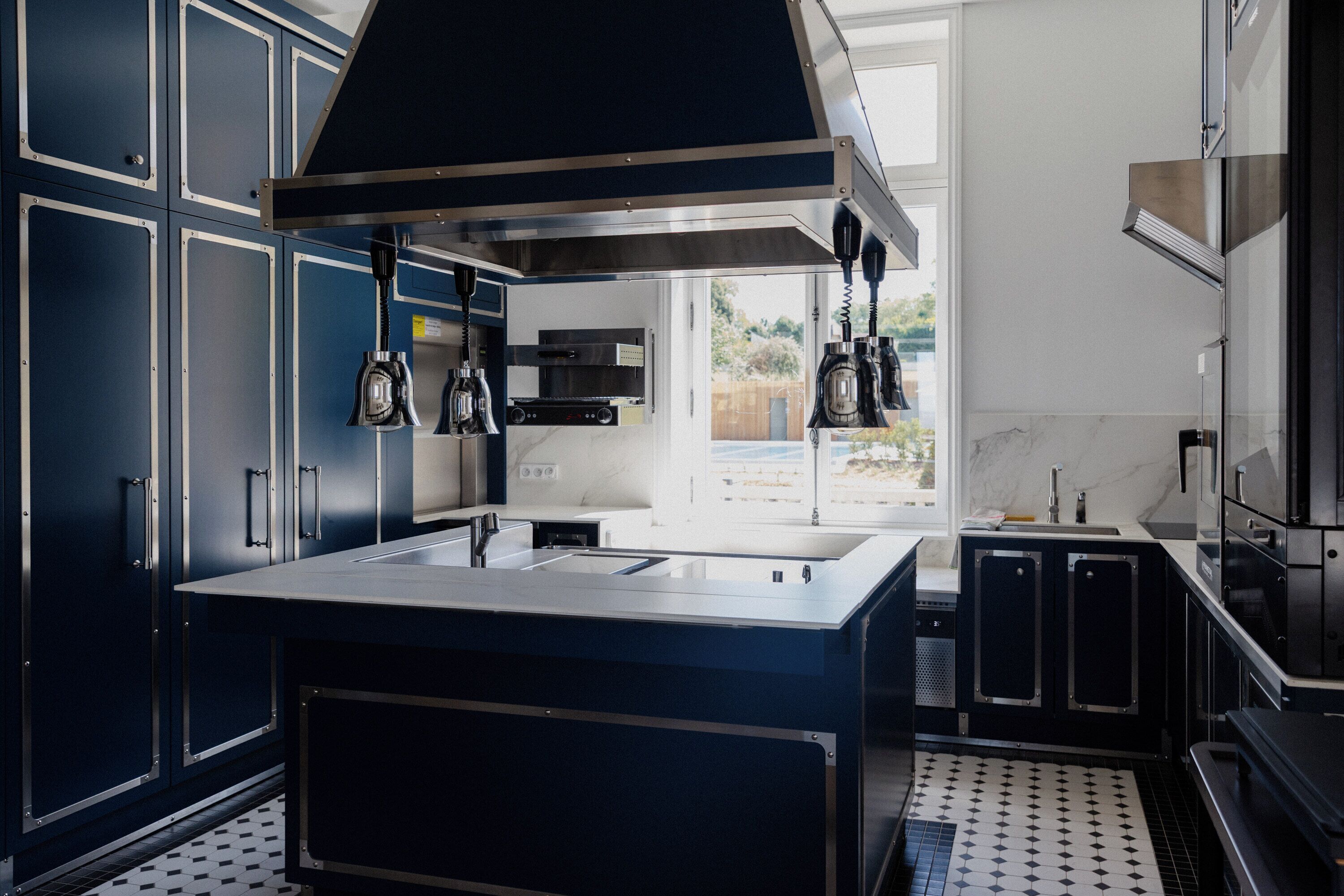 A modern kitchen with dark cabinetry, a central island, and a large window providing a view of the outdoors.