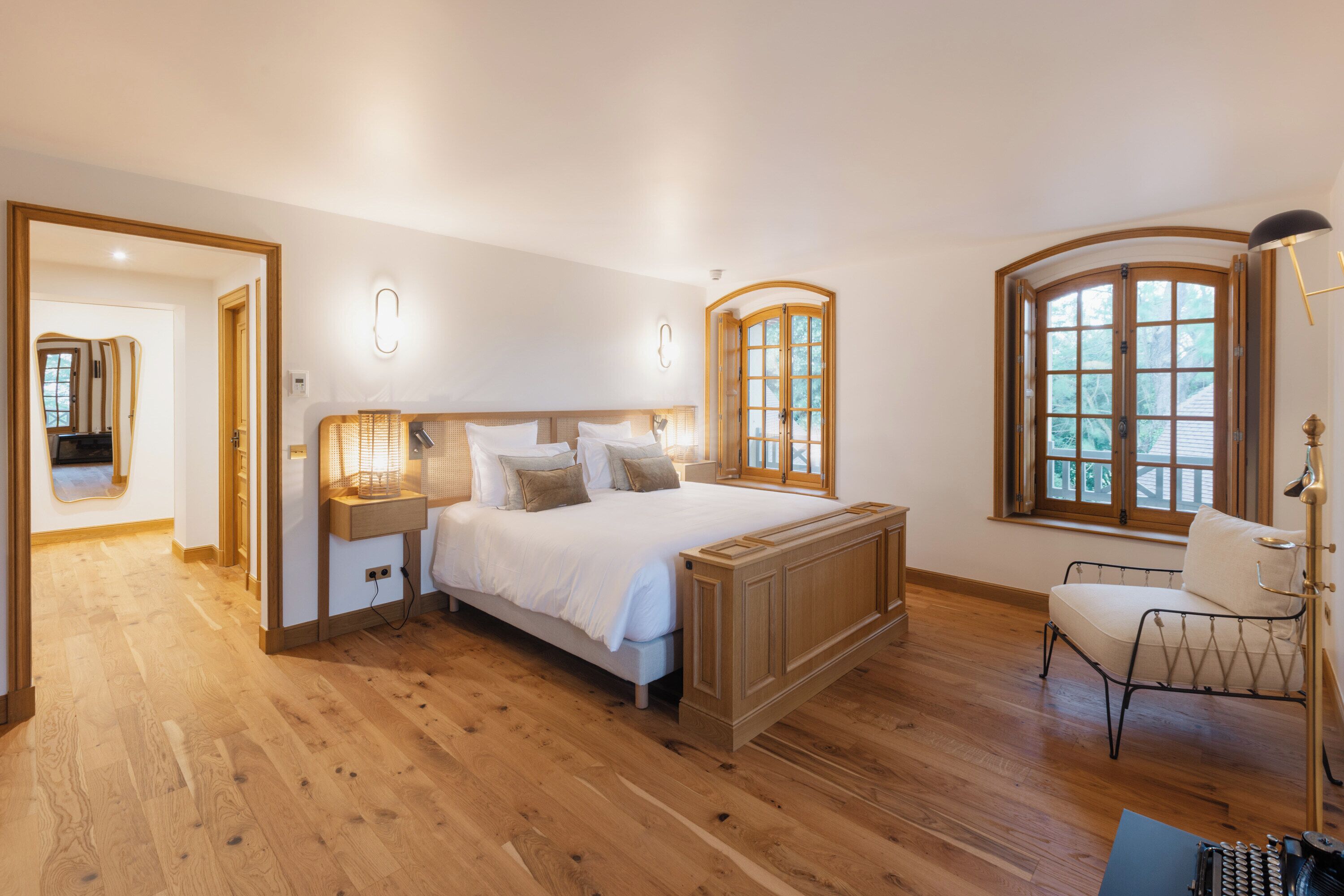 Une chambre spacieuse avec un grand lit, un plancher en bois et une vue sur l’extérieur par une fenêtre.