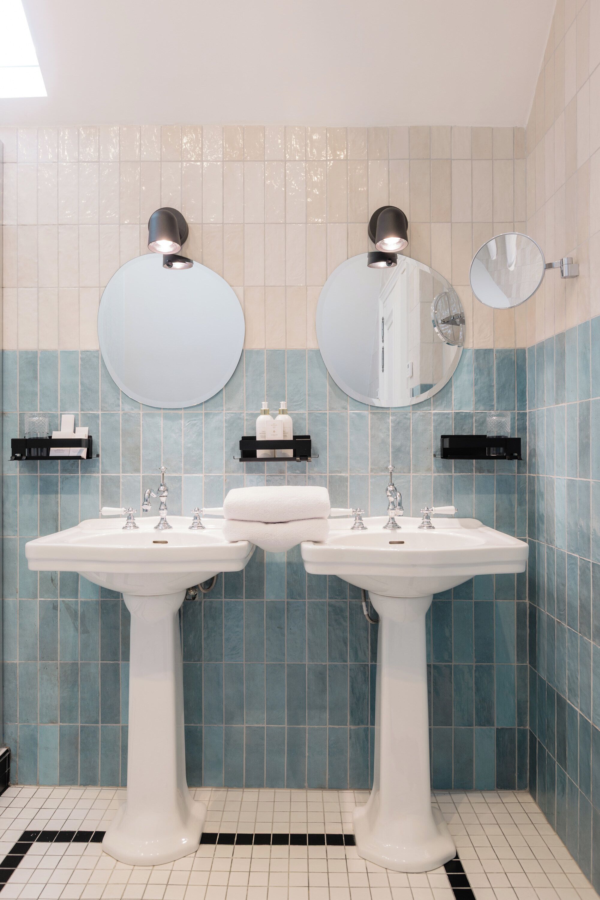 Ein Badezimmer mit zwei Waschbecken, zwei Spiegeln und einer gefliesten Wand.